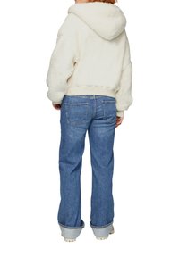 Cremfarbener Fleece-Hoodie mit Kapuze, kombiniert mit hellblauen geraden Jeans. Die Kapuze hat eine weiche Textur; die Jeans verfügen über Gesäßtaschen.