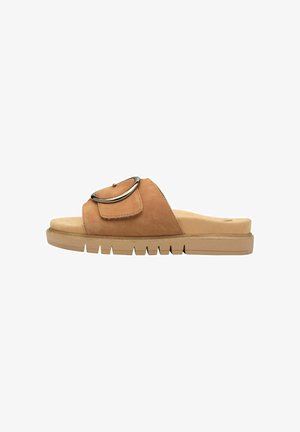 Tan suede slide-sandaalit, joissa on metallinen rengasakseli, litteä pehmustettu pohja ja uurretut kumipohjat paremman pidon saavuttamiseksi.