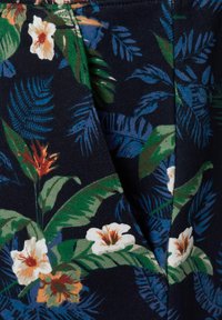 Tessuto con motivo floreale che presenta foglie tropicali e fiori bianchi su uno sfondo blu navy scuro; texture morbida con una leggera lucentezza.