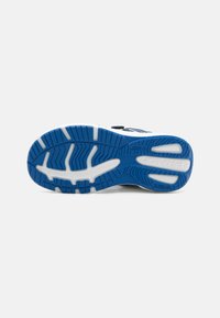 Semelle en caoutchouc texturé de chaussure de sport bleue. Comprend une semelle intermédiaire blanche et des rainures pour la traction, avec des détails et des logos visibles.