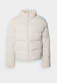 Jachetă puf cu culoare crem, cu guler înalt, model de cusături orizontale, fermoar frontal și mâneci ușor scurte. Material rezistent la apă.