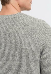 Sivi rebrasti pleteni pulover z okroglim izrezom, teksturirano tkanino in vidnimi šivi ob rami, kar ustvarja oprijet silhueto.