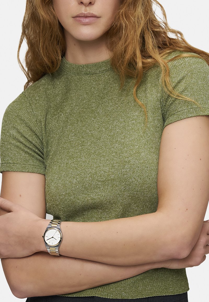 Grön ribbad stickad topp med kort ärm och rundad halsringning. Inkluderar en klocka i silver och guldton med vit urtavla och tre visare.