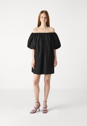 Svart av-ned skuldra kjole med puff-ermer, knelengde. Kombinert med lilla stroppede høye hæler. Glatt stoff, minimalt design.