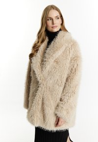 Faux fur frakke i lys beige, med sjalkrave, oversized pasform og struktureret stof. Kombination med en sort turtleneck og ribbet nederdel.