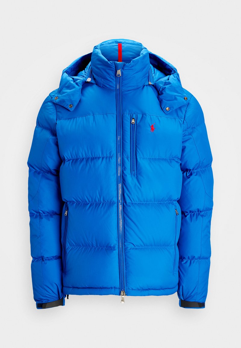 Blue puffer jacket with a zip front, hood, and red accent on the collar. Features quilted design and logo on the left chest.