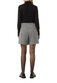 Black turtleneck paired with grey houndstooth shorts; shorts feature a textured finish and a tailored fit, complemented by black shoes.