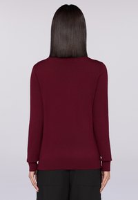 Burgunderfarbener gestrickter Pullover mit langen Ärmeln und rundem Halsausschnitt. Mit einem gerippten Saum und Bündchen, glatter Textur, ohne sichtbare Muster.