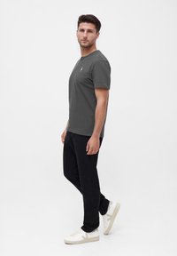 Kurzärmliges, dunkelgraues Baumwoll-T-Shirt mit Rundhalsausschnitt. Kombiniert mit schwarzen Jeans und weißen Turnschuhen mit beigen Akzenten. Einfaches Design.