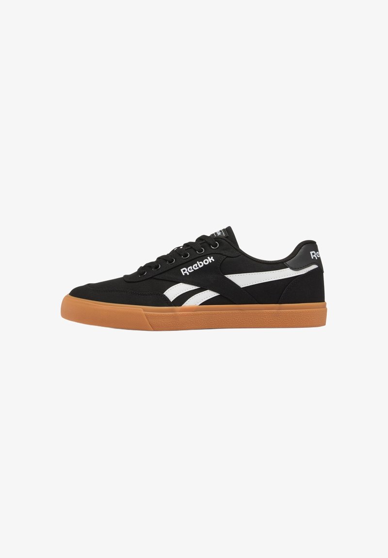 Zapatilla Reebok negra de perfil bajo con rayas laterales blancas, suela de goma color caramelo y cordones negros, mostrada de perfil sobre fondo blanco.