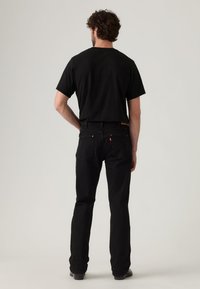 Μαύρο τζιν και μαύρο μπλουζάκι, ορατά από πίσω. Το τζιν έχει κλασική κοπή, με λεπτές ραφές και ένα λογότυπο κοντά στη μέση.