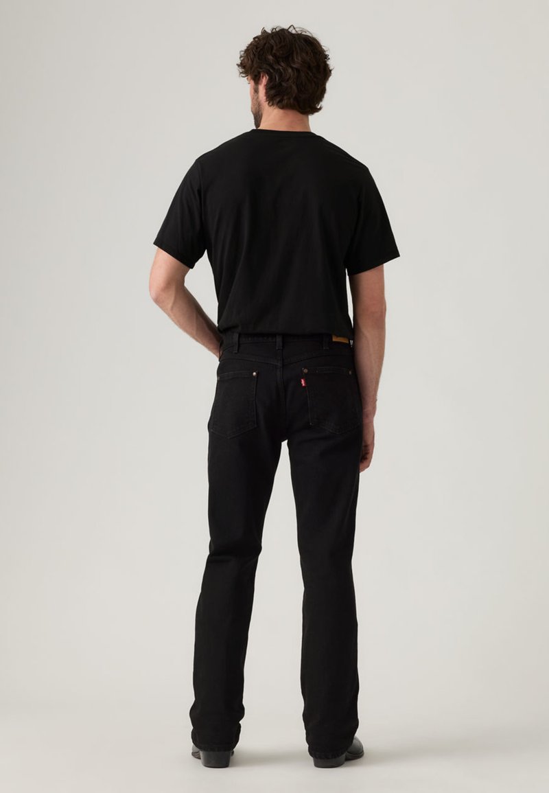 Jeans neri e una maglietta nera, visti da dietro. I jeans hanno un taglio classico, con cuciture sottili e un'etichetta con il logo vicino alla vita.