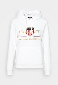 Felpa bianca con cappuccio, cordini, tasca frontale a marsupio e logo scudo ricamato rosso e blu. Presenta il testo dorato "GANT" e "AMERICAN SPORTSWEAR."