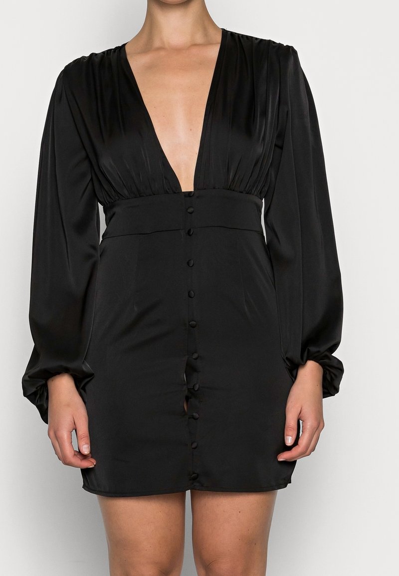 Musta mini-mekko silkkisestä kankaasta, syvällä V-kaulaaukolla, pitkät puffihihat ja etuosassa napitusta kiinnitystä varten.