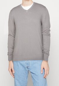 Gray knitted sweater with a V-neck, long sleeves, and ribbed cuffs, worn over a white T-shirt, paired with light blue jeans.