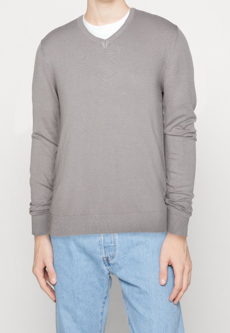 Gray knitted sweater with a V-neck, long sleeves, and ribbed cuffs, worn over a white T-shirt, paired with light blue jeans.