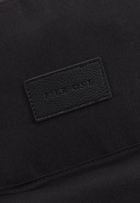 Sac en tissu noir avec une étiquette en cuir texturé embossée du texte "PIER ONE." Présente une finition lisse et un subtil détail de couture.