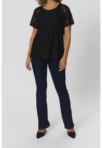 Svart topp med spetskort ärm, med ett strukturerat mönster. Bärs tillsammans med mörkblå utsvängda jeans och svarta spetsiga klackar.