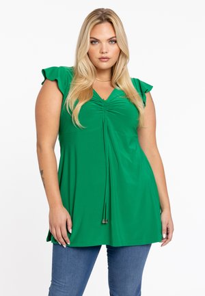 Groene top met korte mouwen, geplooide halslijn en trekkoorddetail. Gemaakt van een gladde stof. Gecombineerd met spijkerbroek.