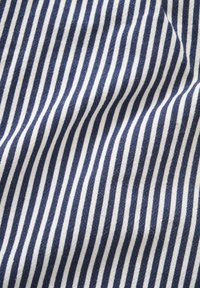 Gros plan sur un tissu doux avec des rayures verticales bleu marine et blanches régulièrement espacées, montrant des plis doux et la texture.
