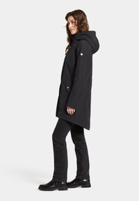 Svart vattentät parka med huva, framfickor och tryckknappar; stylet med svarta jeans och stövlar för en komplett look.