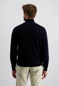 Navyblauwe polo met lange mouwen, voorzien van een ribbelkraag en -manchetten, met een soepele textuur en een getailleerd ontwerp, gecombineerd met lichtgekleurde corduroypantalons.