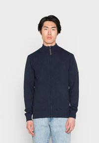 Marine blauwe zip-up trui van gebreid materiaal, met een hoge kraag, geribbelde manchetten en een subtiele logo detail op de linker mouw.
