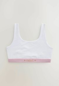 Valkoinen puuvillainen crop-top, leveillä olkaimilla ja vaaleanpunaisella nauhalla helman kohdalla, jossa on sanat "next" kultafoliolla. Sileä pinta.