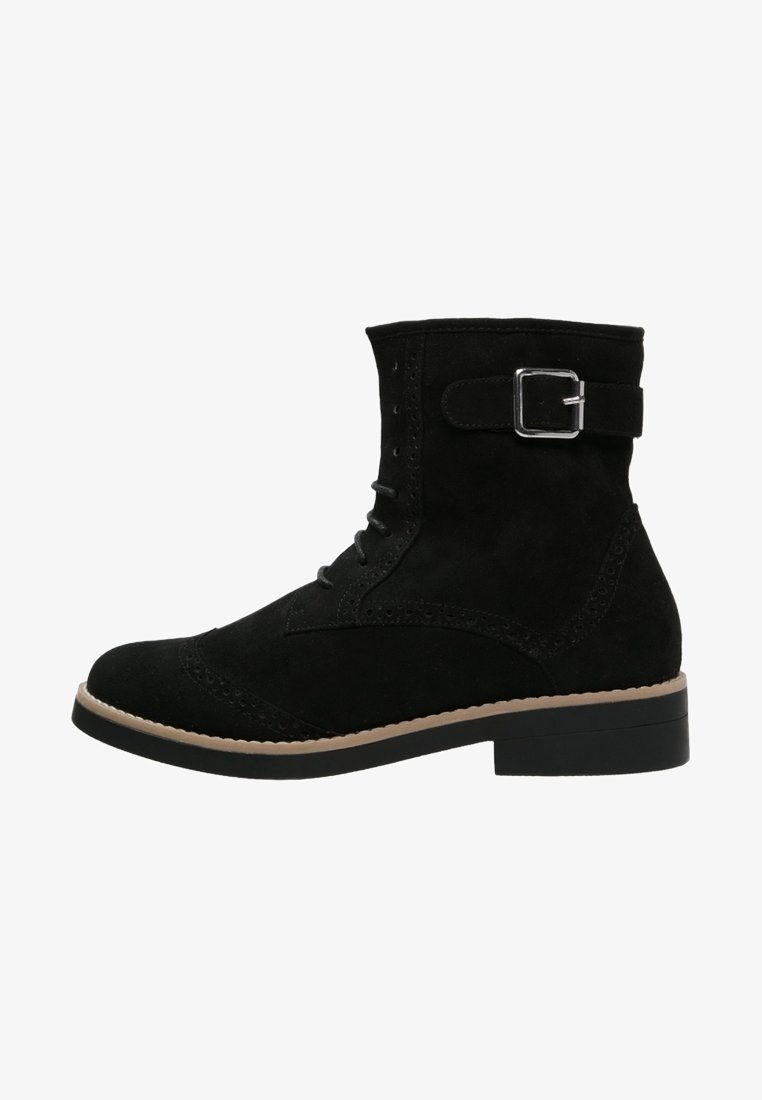 Bottine en daim noir avec laçage à l'avant, perforations décoratives, sangle avec boucle argentée, tranche beige et talon bas empilé.