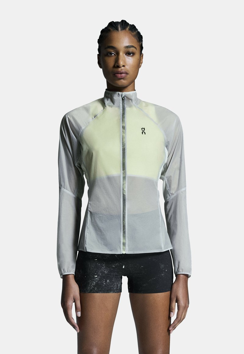 Chaqueta ligera y translúcida en color amarillo pálido y gris. Cuenta con un alto cuello, cremallera completa y un ajuste atlético con mangas largas.