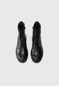 Botas de cuero negro con punta redondeada, tobillo texturizado, suela de goma gruesa y cordones metálicos para un ajuste seguro. Cuenta con un cierre lateral con cremallera.