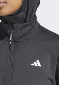 Maglietta da corsa nera con colletto alto, chiusura con zip e logo bianco. Tessuto liscio con dettagli di cucitura sottili. Materiale traspirante progettato per le prestazioni.