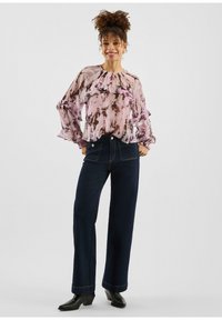 Paarsroze blouse met patroon en geruite mouwen, gecombineerd met hooggetailleerde donkerblauwe wijde broekspijpen en zwarte enkellaarsjes.