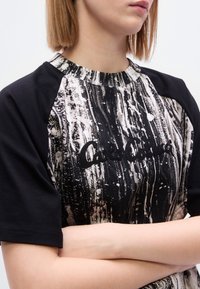 Μαύρο κοντομάνικο μπλουζάκι με σχέδια και στρογγυλή λαιμόκοψη, με υφασμένο τύπωμα και κεντημένο λογότυπο στο μπροστινό μέρος.