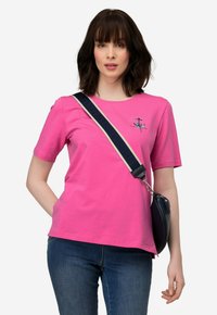 Fuchsia katoenen t-shirt met korte mouwen en een ronde hals. Bevat een geborduurd ontwerp in het blauw. Gecombineerd met blauwe jeans en een schoudertas.