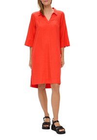 Rotes Leinenkleid mit V-Ausschnitt, Dreiviertelärmeln, seitlichen Schlitzen und gefälteltem Detail. Getragen mit schwarzen Plateausandalen.