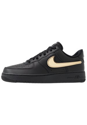 Baskets basses noires avec lacets noirs et grand logo Nike swoosh beige sur le côté, sur fond blanc.