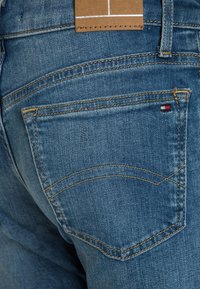 Jeans i denim har en medelblå tvätt, guldstickning och en liten patch med röda, vita och blå detaljer på bakfickan.