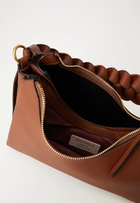 Brown leather handbag with a braided handle, gold zipper, and interior label reading "Coccinelle Authentic Italian Leather."