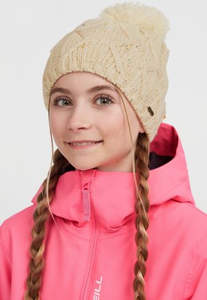 Stickad krämfärgad mössa med ett strukturerat mönster och en pom-pom på toppen. Bärs tillsammans med en klar rosa jacka med hög krage och dragkedja.