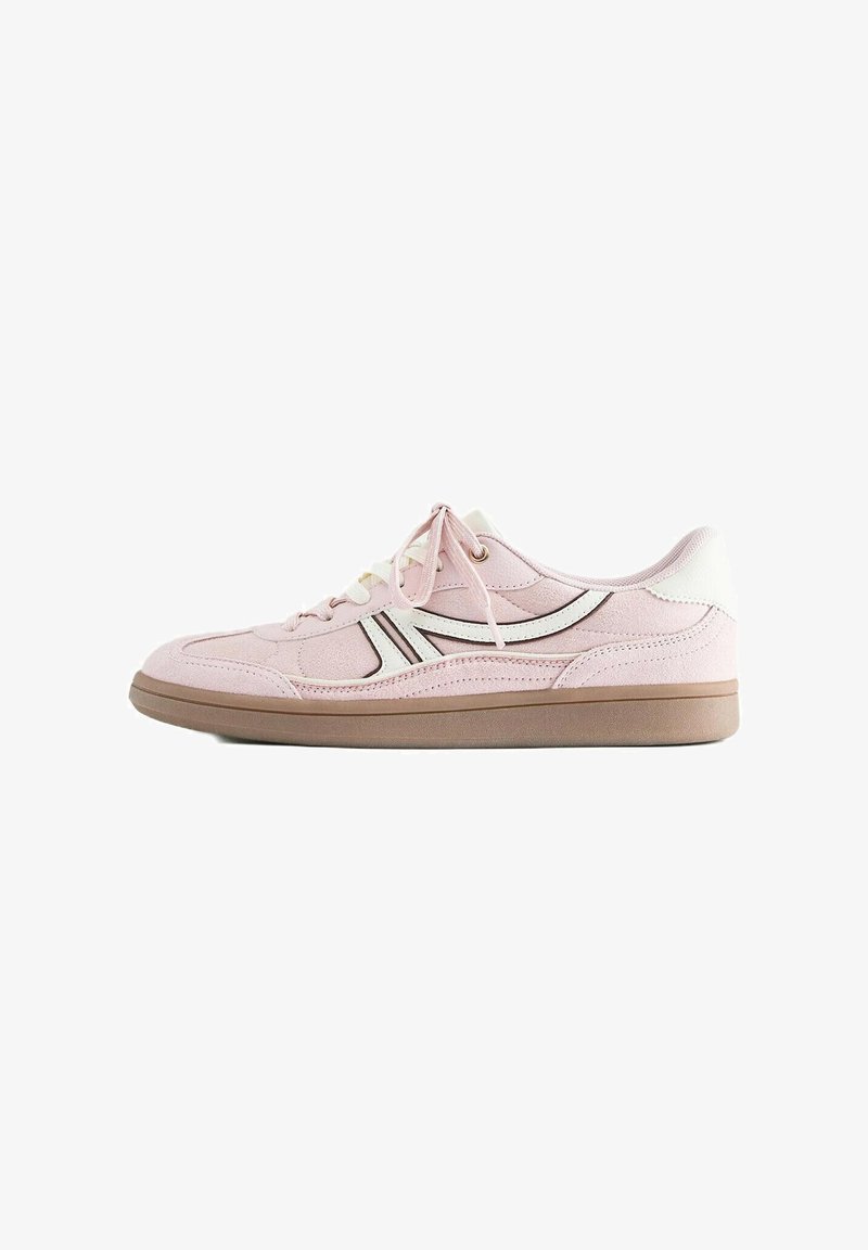 Baskets en daim rose clair avec bandes latérales blanches et noires, lacets blancs, languette de talon blanche et semelle en caoutchouc marron sur fond blanc.