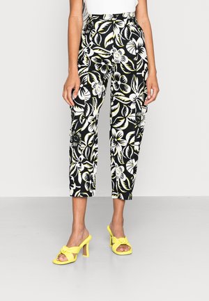Woman wearing black and white floral cropped pants with yellow accents and yellow heeled sandals with bow details.