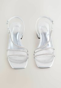 Silberne metallische Absatzsandalen mit quadratischer Zehenform, die drei dekorative Riemen mit kleinen Strasssteinen und einen verstellbaren Knöchelriemen aufweisen.