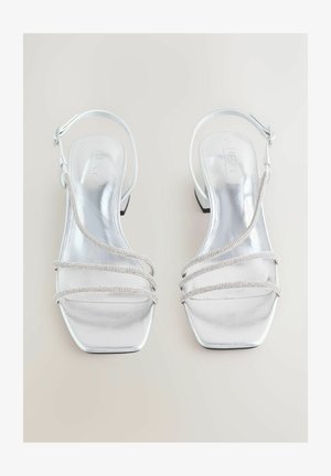 Hõbedased metallilised kontsakingad ruudukujulise varbaga, millel on kolm dekoratiivset rihma, kaunistatud väikeste klaaskristallidega ja reguleeritav pahkluu rihm.