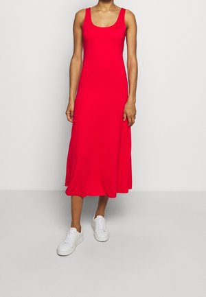 Röd ärmlös midiklänning med rundad halsringning, tillverkad av mjukt material, med en avslappnad passform, matchad med vita sneakers mot en enkel bakgrund.