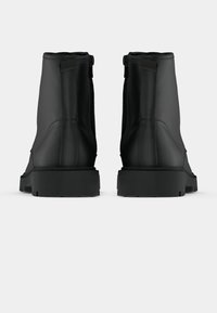 Cizme negre până la gleznă, cu un finisaj neted, prezentând un fermoar pe lateral, un panou posterior texturat și tălpi groase din cauciuc negru.