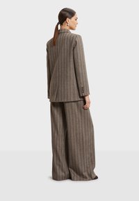Brown gestreepte pakset met een lange blazer in een getailleerde pasvorm en wijde broekspijpen. Gemaakt van gestructureerde stof met een subtiele glans.