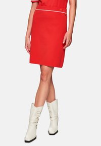 Roter Bleistiftrock mit weißem Saum an der Taille, kombiniert mit weißen Cowboy-Stiefeln mit spitzer Zehe, verziert mit dekorativen Riemen und Akzenten.