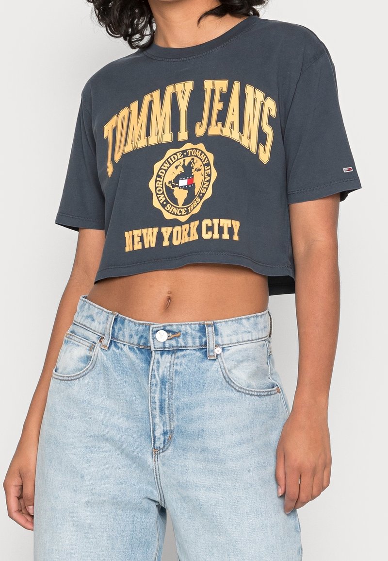 Zkrácený námořnický modrý tričko s žlutým nápisem "TOMMY JEANS" a logem glóbu. V kombinaci s lehkými denimovými vysokými džíny se zapínáním na knoflík.