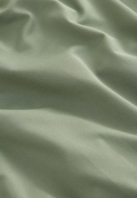 Tissu doux vert clair avec un fin tissage diagonal, présenté en plis doux et texture lisse.